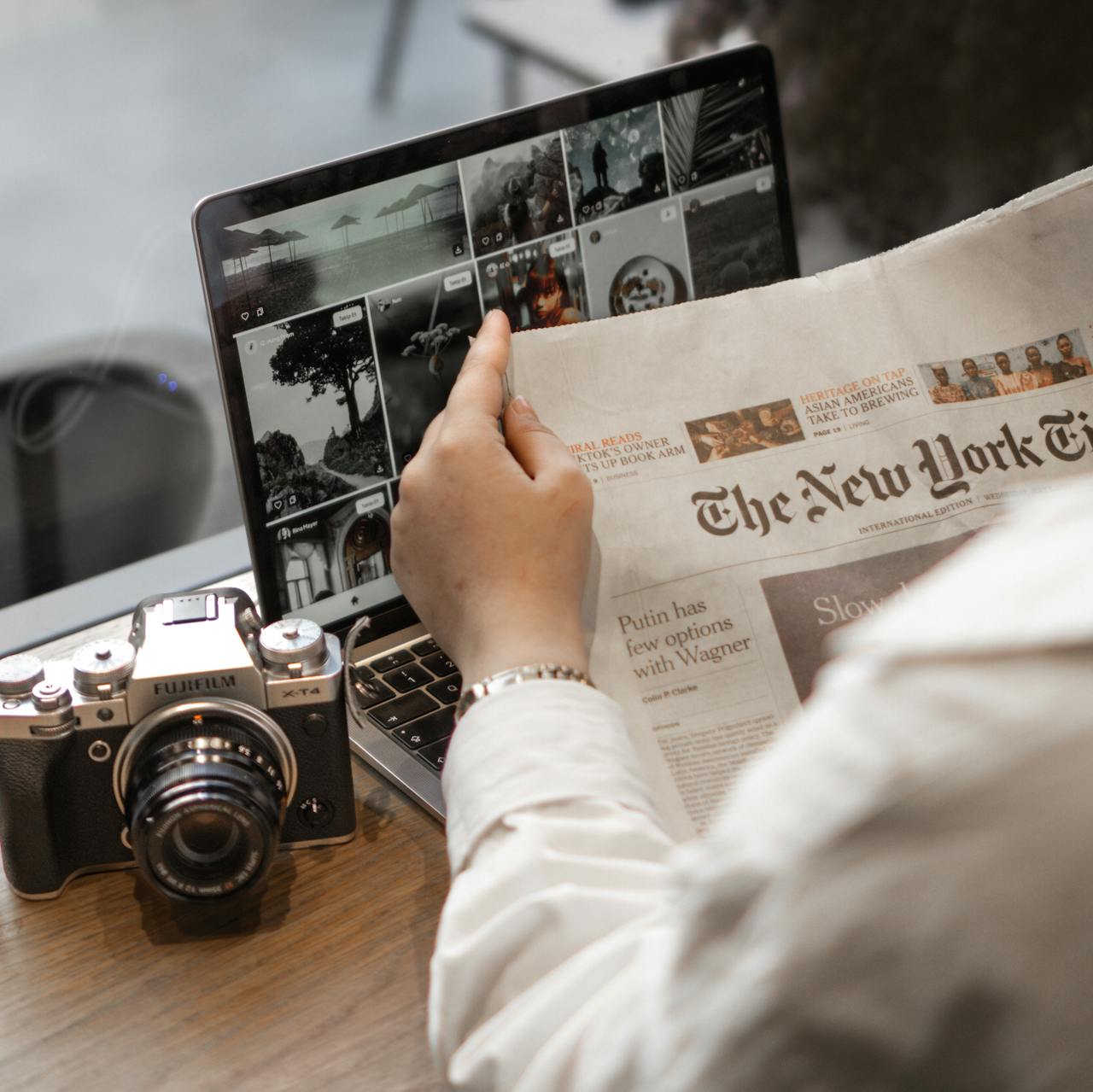 Close-up of a person reading The New York Times by a laptop and camera.